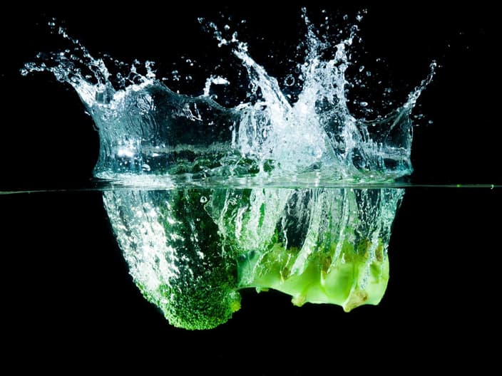 Salting the greens keeps them green - Green broccoli falling in water on white with air bubbles