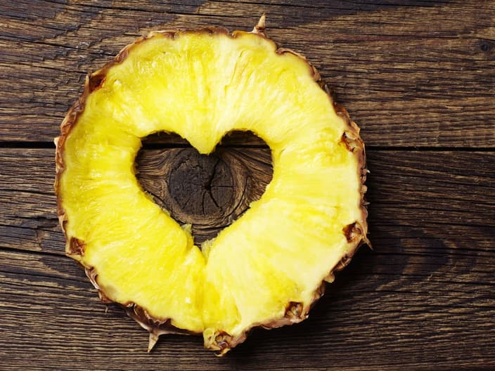 Sliced pineapple with a cut in shape of hearts on vintage wooden background