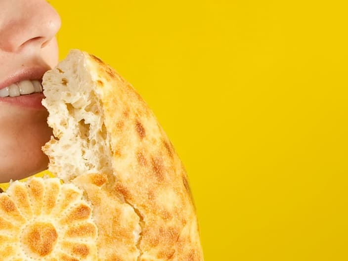female baker is smelling fresh loaf over yellow