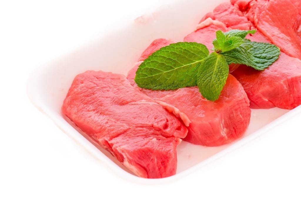 Supermarket packaged porterhouse steaks with mint leaf isolated against a white background