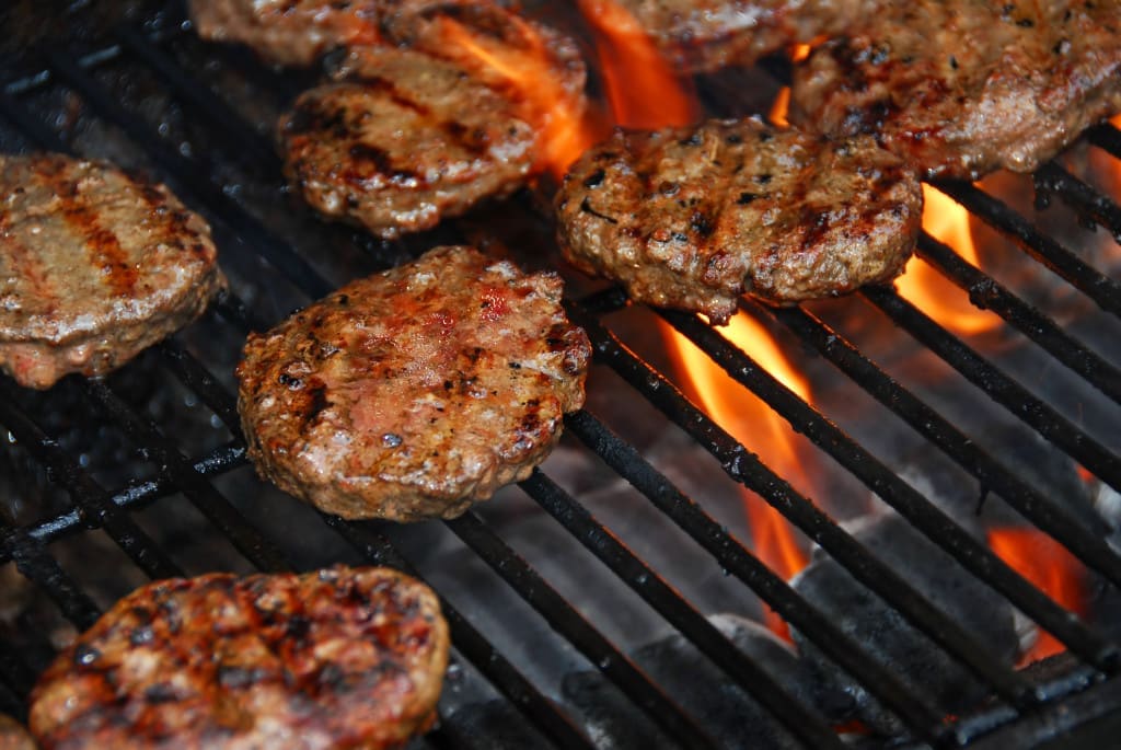 Burgers cooking on barbeque grill with coals and flames