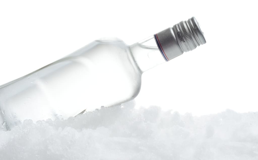 Close-up view of bottle of vodka lying on ice on white