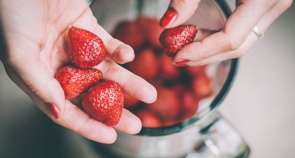 Hands putting fresh strawberries in blender cup. Selective focus. Toned image