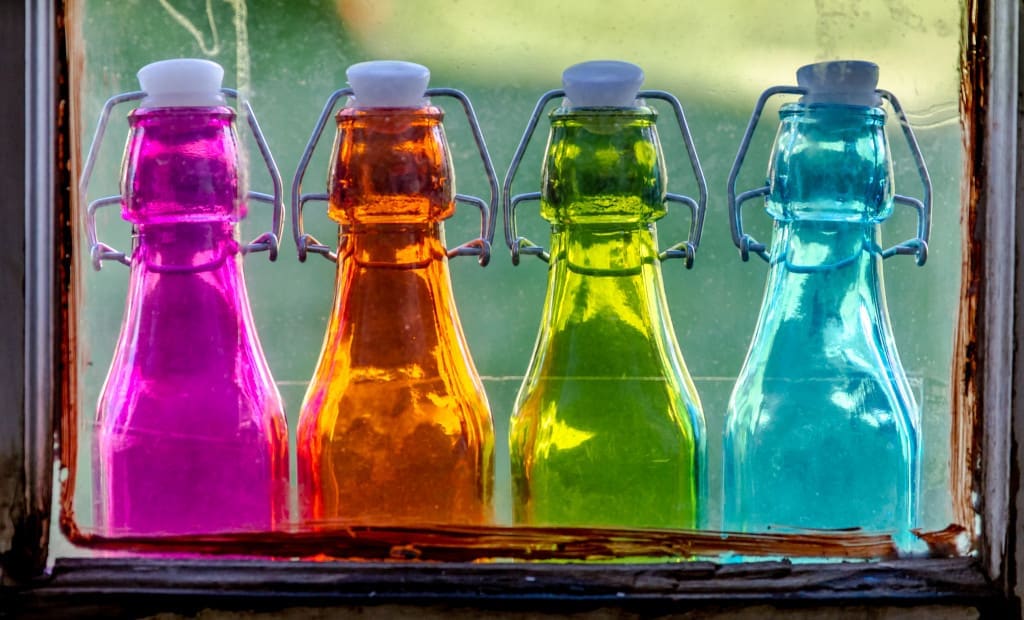 Close up of colored vintage bottles sitting on wooden window sill through old glass window