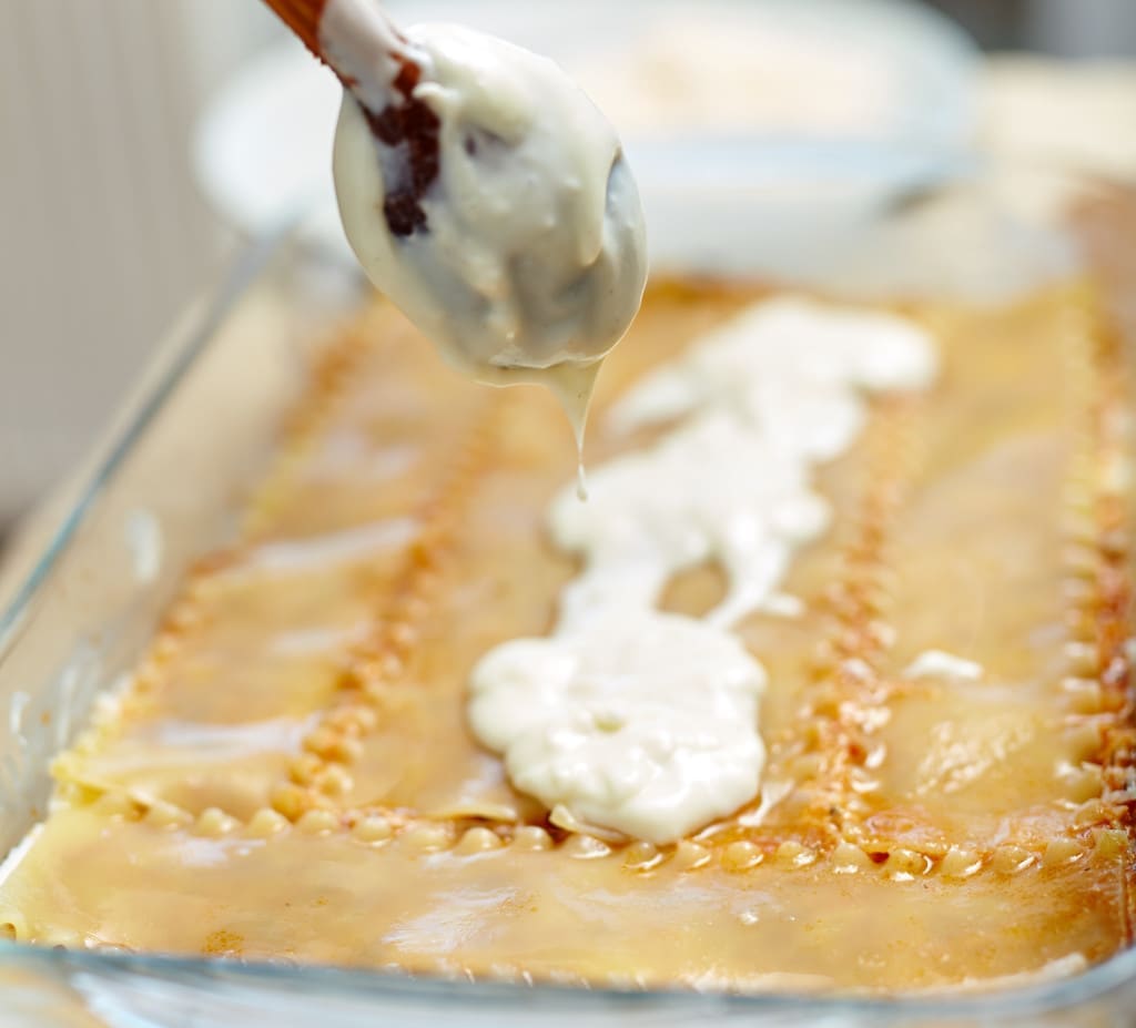 Woman spreading bechamel sauce - made with roux and milk - on lasagna pasta in a tray