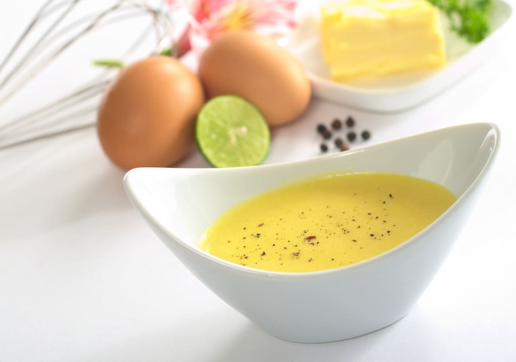 Hollandaise sauce with black pepper and the ingredients (butter, egg, lemon) of the sauce in the back (Selective Focus, Focus in the middle of the bowl)
