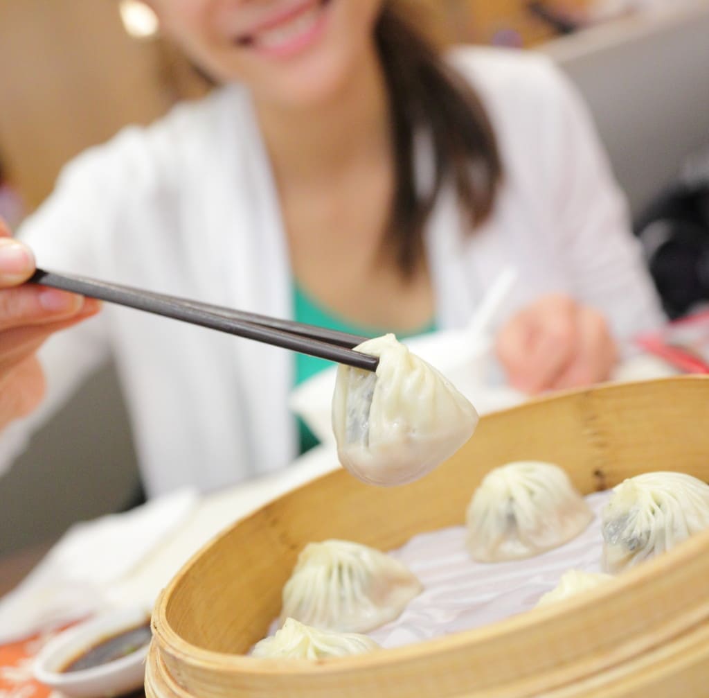 Xiao long bao / xiaolongbao soup dumplings. Woman eating Chinese Shanghainese steamed dumpling buns with chopsticks in restaurant in China.