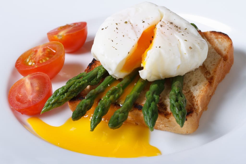 Simmering is best for poaching eggs - Toast with asparagus, poached egg and tomato on a white plate closeup. horizontal