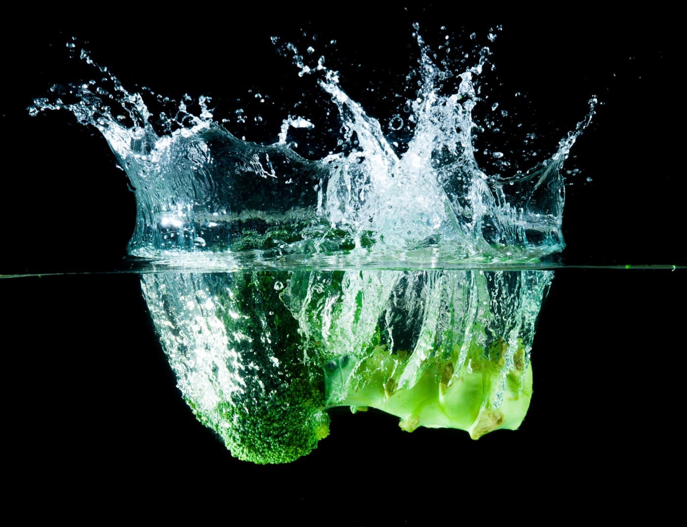 Salting the greens keeps them green - Green broccoli falling in water on white with air bubbles