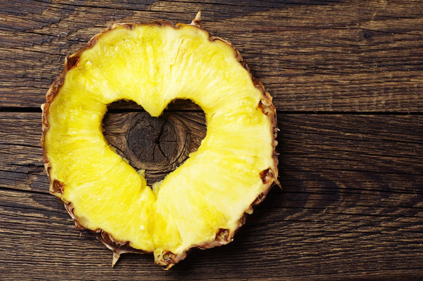Sliced pineapple with a cut in shape of hearts on vintage wooden background