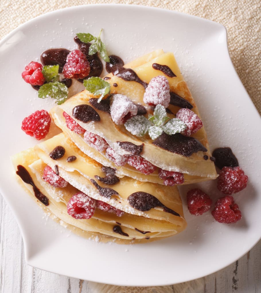 raspberry crepes with chocolate and mint close-up on a plate. Vertical view from above