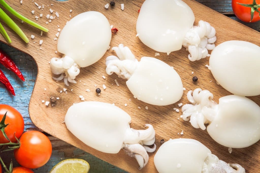Raw babies cuttlefish on a cutting board with tomatoes, onions, chili peppers and lemon closeup