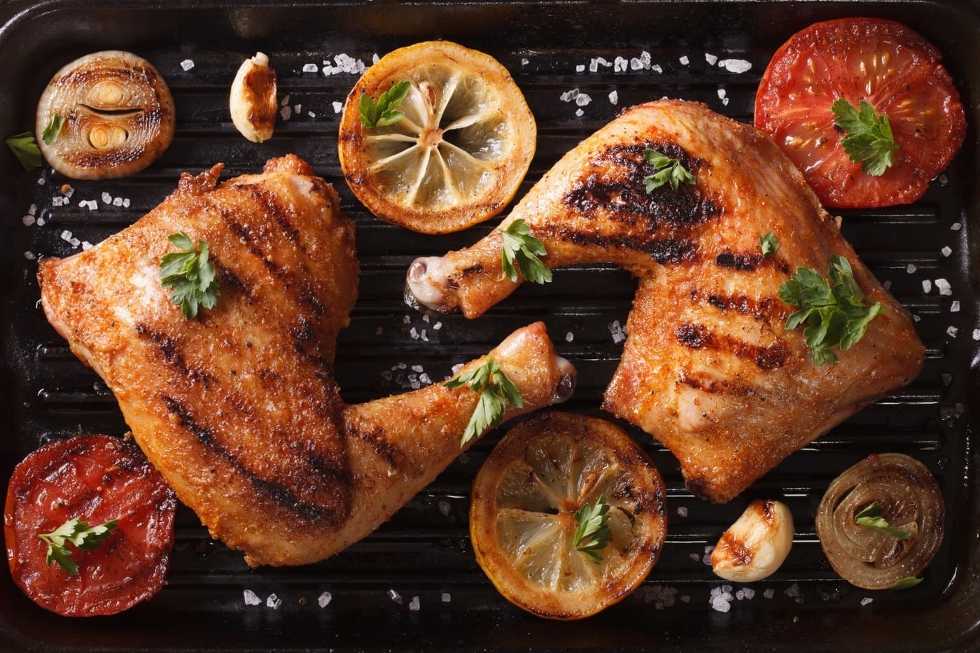NaCl - brining makes meat juicier - Two grilled chicken legs and vegetables on the grill pan close-up. horizontal view from above