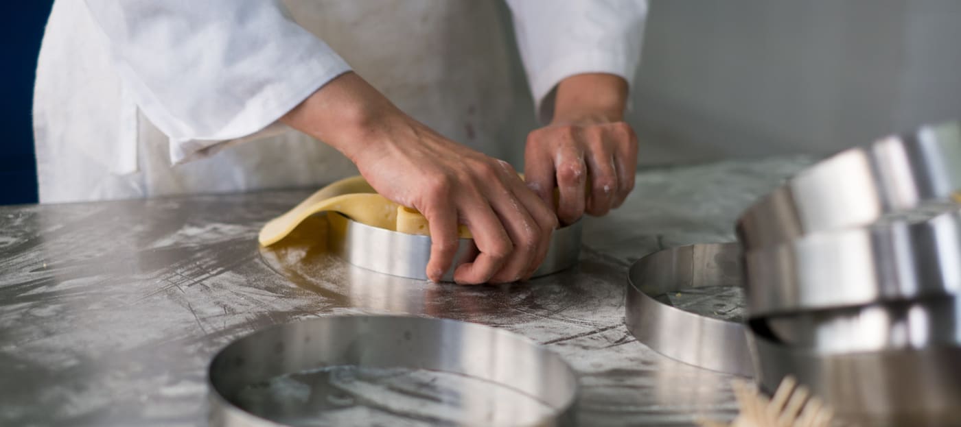 a stainless steel top is an even better conductor of heat - Pastry chef's hands pulling pit dough into a stainless steel pie crust ring sitting on flour dust covered stainless steel prep table.
