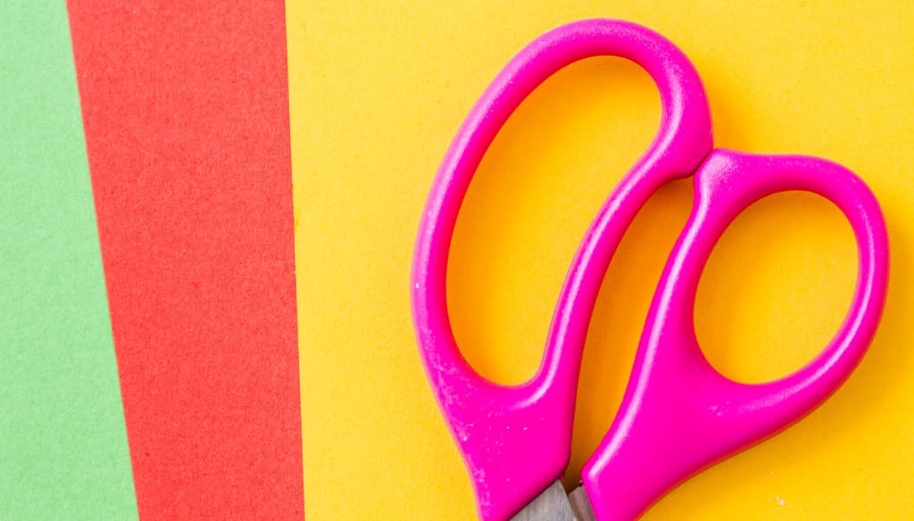 colorful handles make a pair of scissors easy to find and an iconic look - Pink scissors and colorful handicraft papers, top view