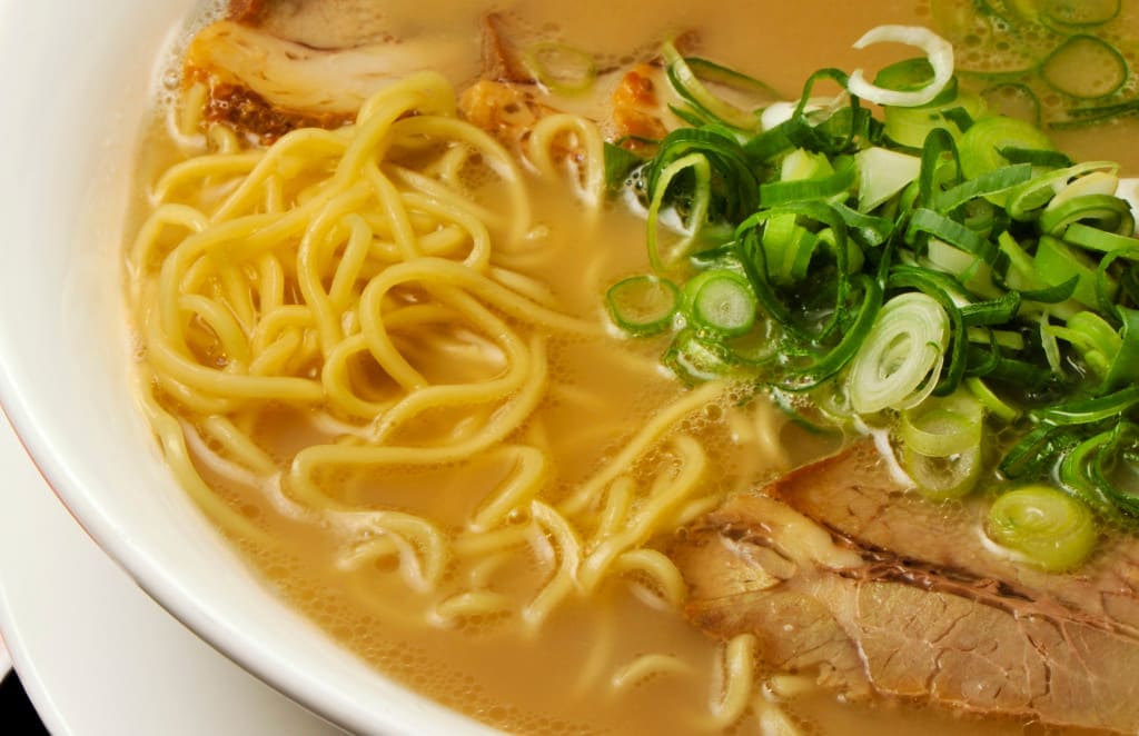 close up of bowl of japanese ramen with pickles on the side