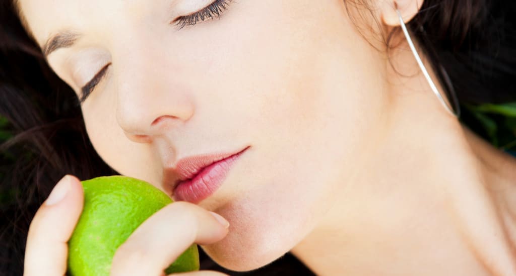 Pretty brunette girl wearing elegant dress relaxing outdoor in green grass and smells aromatic lemon or lime citrus