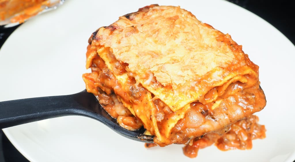 Plating fresh lasagna onto porcelain plate with black spatula