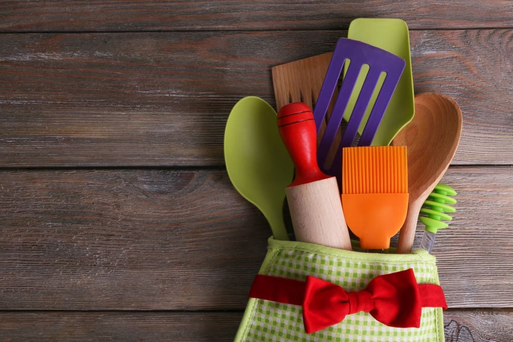 Silicone spatula in a Set of kitchen utensils in mitten on wooden planks background